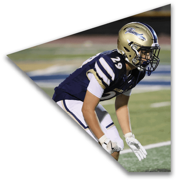 A person wearing a football uniform with the number 29 and a gold helmet is crouched on a field, appearing ready to play. Description generated by AI