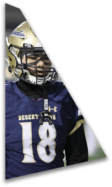A person wearing a football helmet and a blue jersey with the number 18 and the word Desert Vista is standing on a field. Description generated by AI