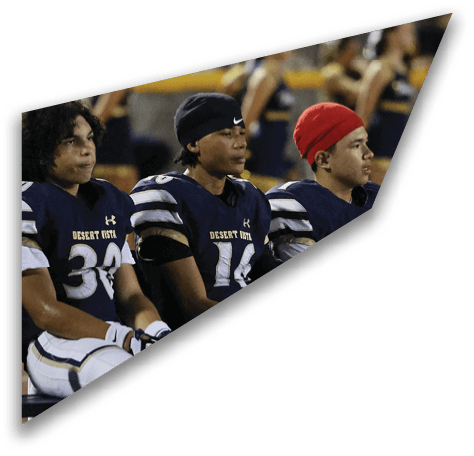 Three people wearing football uniforms with “Desert Vista" on the jerseys are sitting side by side on a bench during a game. Description generated by AI