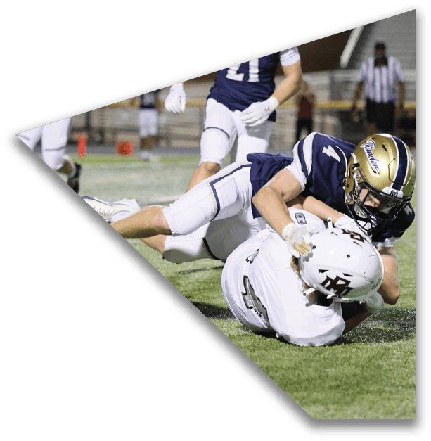 People in football uniforms are engaged in a tackle on a grassy field during a nighttime game. Description generated by AI