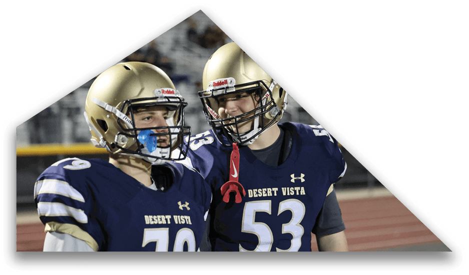 Two people wearing Desert Vista football uniforms and helmets are standing close together on a sports field. Description generated by AI