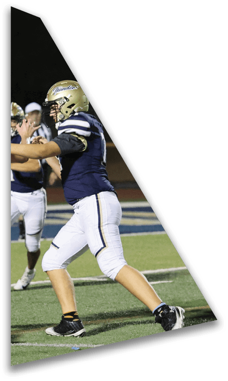 An adult in a football uniform is preparing to throw a football on a field with another player in the background. Description generated by AI