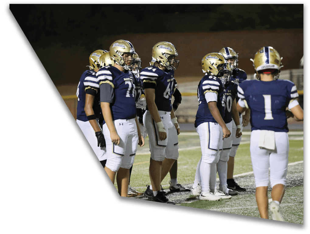 A group of people wearing football uniforms and helmets stand together on a field during a nighttime game. Description generated by AI