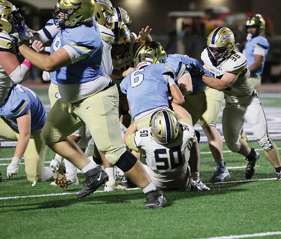 Several people in football uniforms are engaged in a play on a green field with one person wearing a jersey numbered 50 on the ground. Description generated by AI