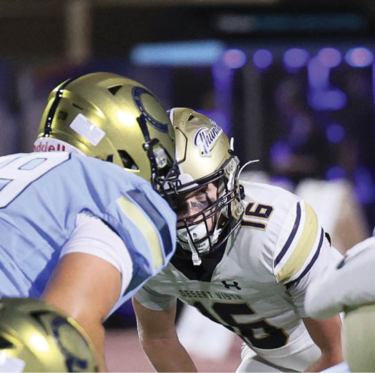 Two people in football uniforms are facing each other closely, appearing ready for a play on the field. Description generated by AI