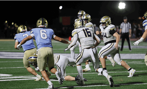 People wearing football uniforms are actively engaged in a play on a well-lit field during a nighttime game. Description generated by AI