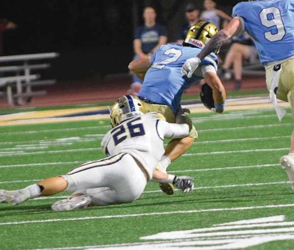 Two football players in blue uniforms and gold helmets are on a field at night near a goalpost. Description generated by AI