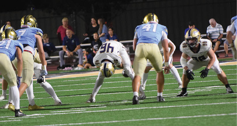 A person wearing a yellow and blue uniform is catching a football near a yellow goalpost at night. Description generated by AI