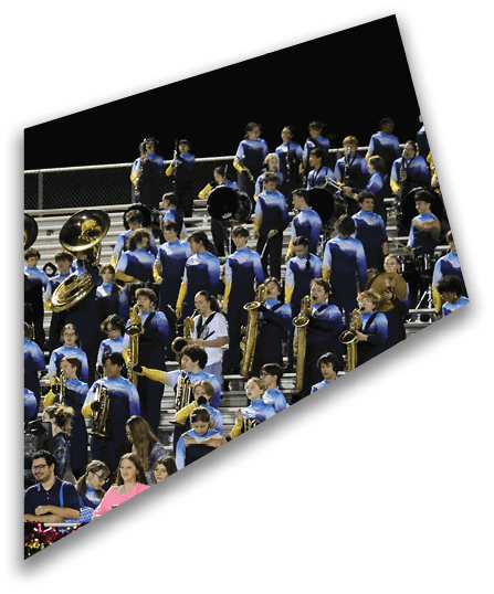 A large group of people in matching blue and black uniforms are seated and standing in bleachers playing various brass and percussion instruments while a few people in casual clothing stand in front of the bleachers. Description generated by AI