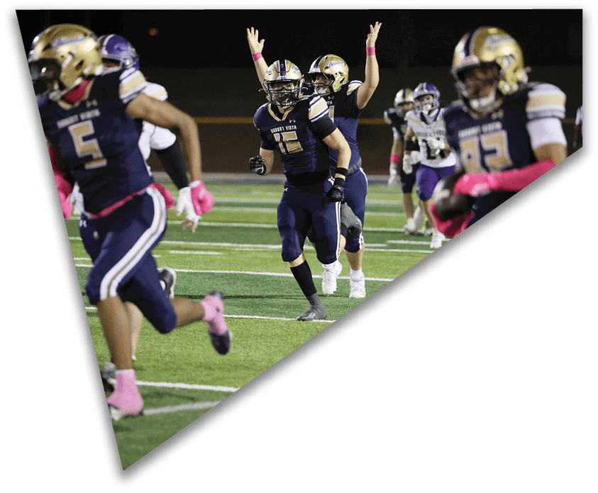 People wearing dark sports uniforms with pink gloves and socks are running on a football field during a game. Description generated by AI
