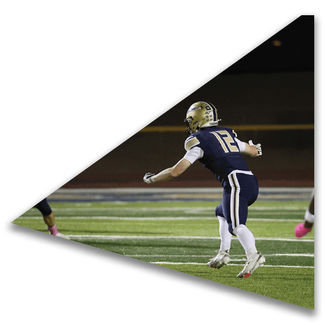 Two people in football uniforms are on a field with one person in mid-jump and the other running nearby. Description generated by AI