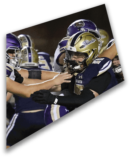 People wearing dark sports uniforms are engaged in a close physical interaction, likely during a football game. Description generated by AI