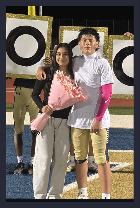 Two people stand close together holding large white signs with black circles outlined in gold glitter, under a yellow goalpost at night. Description generated by AI
