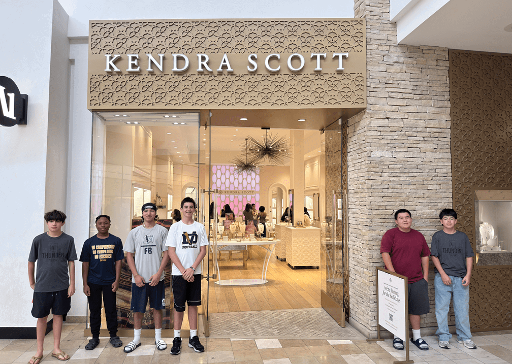 Six people stand in front of a Kendra Scott jewelry store inside a shopping mall, with the store's interior visible behind them. Description generated by AI