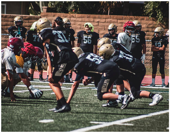 People wearing athletic clothing and cleats are crouched in a ready position on a sports field with artificial turf and white lines. Description generated by AI