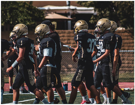 A group of people wearing black sports uniforms and cleats are walking together on a football field. Description generated by AI