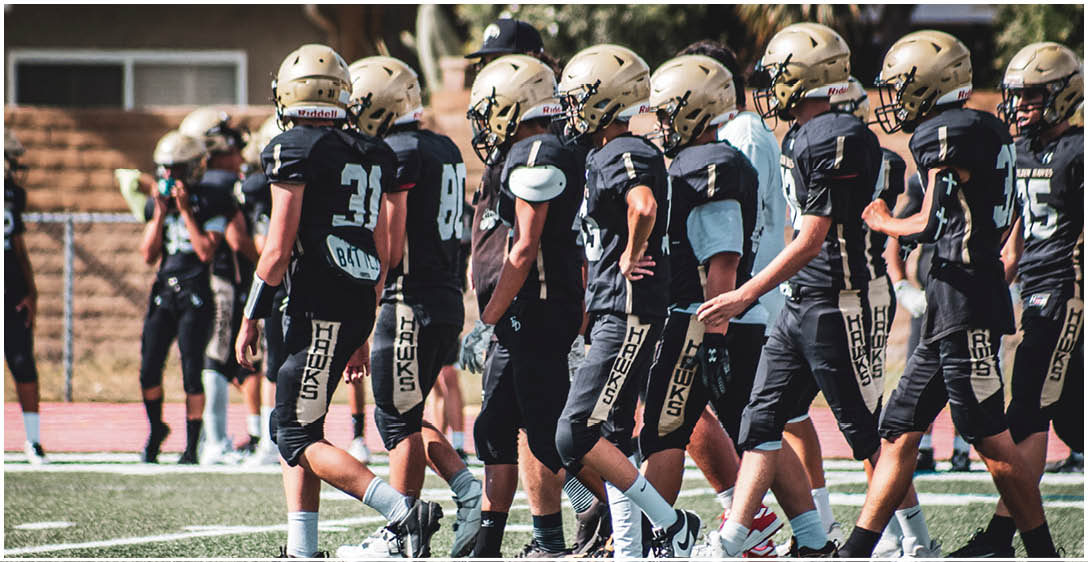 A group of people wearing black football uniforms with “HAWKS" written on their pants are walking together on a sports field. Description generated by AI