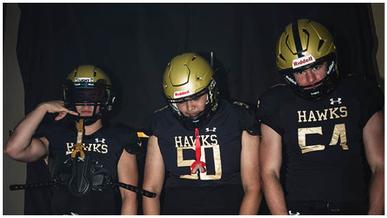 Three people wearing gold football helmets and black jerseys stand in front of a dark backdrop. Description generated by AI