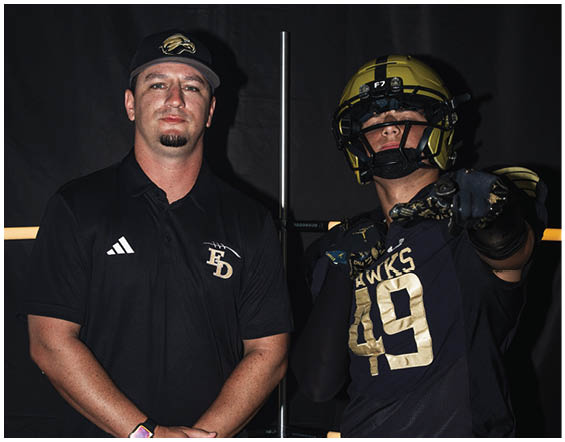 Two adults pose against a dark background with one wearing a black sports polo and cap and the other in a black football uniform and helmet pointing forward. Description generated by AI