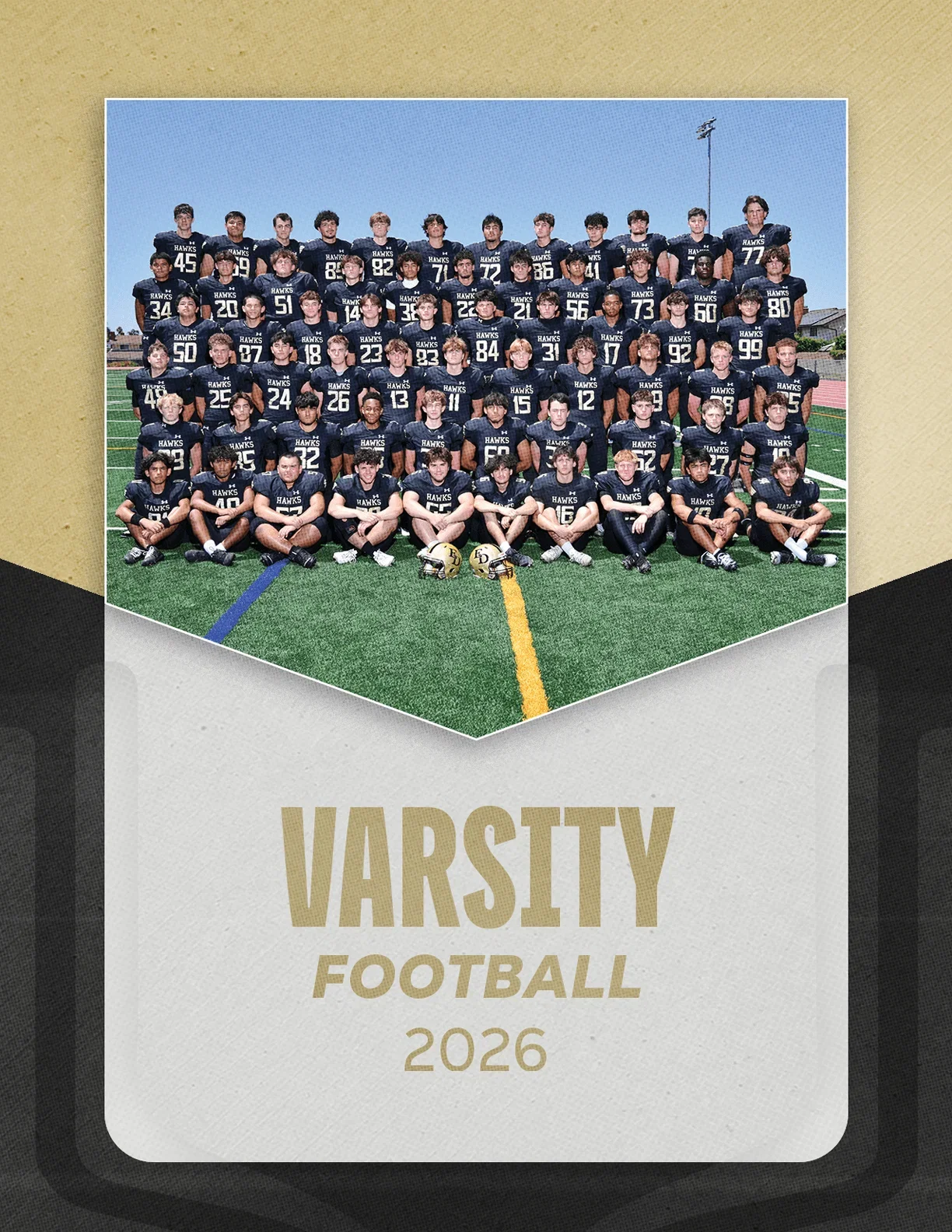 A large group of people wearing matching dark sports uniforms pose together on a football field with the text varsity football 2026 below them. Description generated by AI