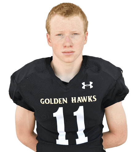Person with curly hair wearing a black football jersey with the word “HAWKS" and the number 38 standing against a gray background. Description generated by AI