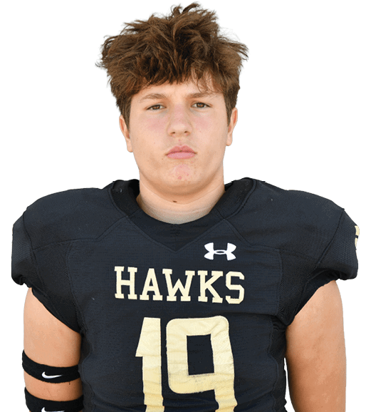 Person with short curly hair wearing a black football jersey with the word “HAWKS" and the number 19 standing against a plain background. Description generated by AI