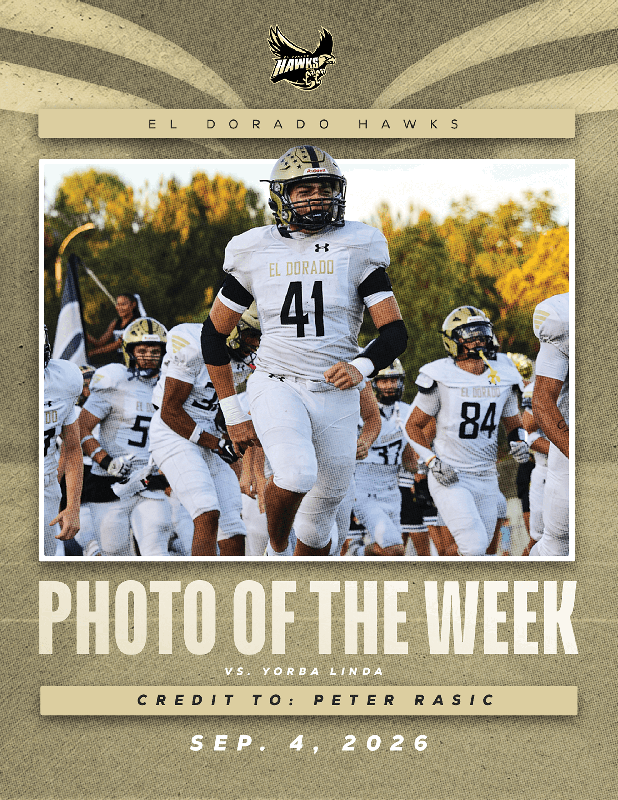 A group of football players in white uniforms with “El Dorado" on the jerseys are running on a field with trees in the background, featured as the photo of the week for a game against Yorba Linda. Description generated by AI