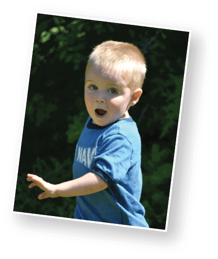 A child with short light hair wearing a blue shirt is outdoors with an open mouth and an expressive face, reaching out with one hand. Description generated by AI