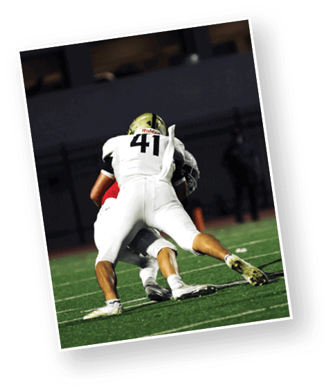 Two people in football uniforms are engaged in a tackle on a well-lit field at night. Description generated by AI