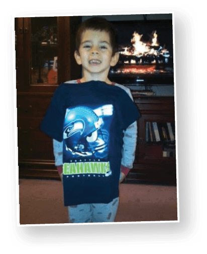 A child with short curly hair wearing a white polo shirt and blue jeans stands in front of a blurred ocean background. Description generated by AI