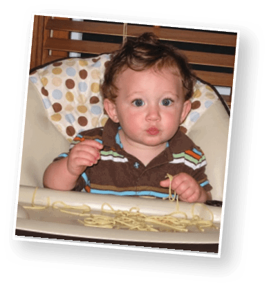 A child with short curly hair wearing a white polo shirt and blue jeans stands in front of a blurred ocean background. Description generated by AI