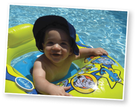 A child with short curly hair wearing a white polo shirt and blue jeans stands in front of a blurred ocean background. Description generated by AI