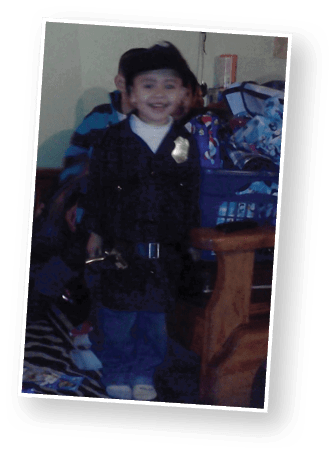 A child dressed in a police costume is smiling while standing indoors with other children and household items in the background. Description generated by AI