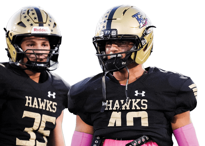 Two people wearing black football uniforms with gold helmets and pink arm sleeves are standing on a field. Description generated by AI