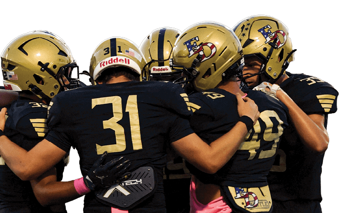 A group of five people wearing black sports uniforms and gold helmets are huddled together on a football field. Description generated by AI