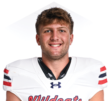 A person with short hair is smiling and wearing a white Wildcats football jersey with red and blue stripes on the sleeves. Description generated by AI