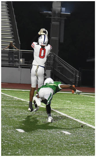 A person in a white football uniform with the number zero is catching a football on a field with bleachers and a spectator in the background. Description generated by AI
