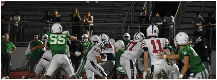 People in football uniforms are engaged in a game on a field with spectators sitting in the bleachers behind them. Description generated by AI