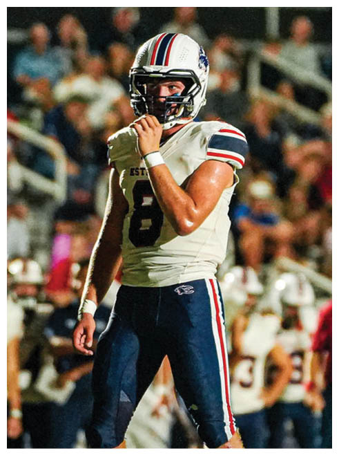 A person wearing a white football helmet with red and blue stripes and a white football jersey is holding their chin strap while looking ahead. Description generated by AI