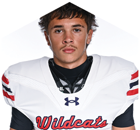 Person with short, tousled hair wearing a white football jersey with “Wildcats" written on it and black undershirt. Description generated by AI