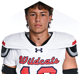 A person with short tousled hair wearing a white Wildcats football jersey and shoulder pads looks directly at the camera against a plain white background. Description generated by AI