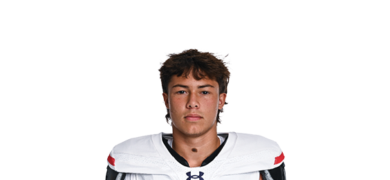 A person with curly hair wearing a white football jersey with red and black accents and the word Wildcats along with the number 10 on the front is standing against a plain white background. Description generated by AI