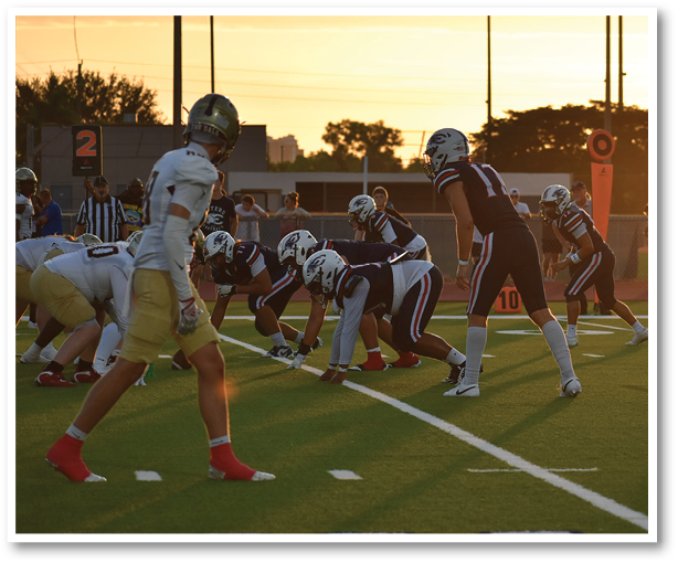 A group of people in football uniforms are lined up on a field at sunset preparing for a play. Description generated by AI