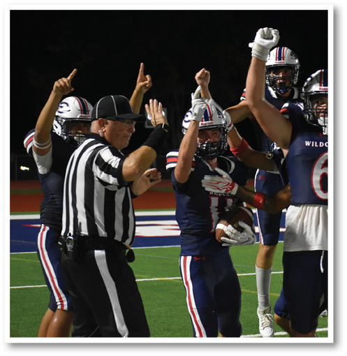 A group of football players in Wildcats uniforms and a referee are celebrating on a field at night. Description generated by AI