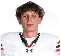A person with curly hair wearing a white sports jersey with red and black stripes and an Under Armour logo is looking directly at the camera. Description generated by AI