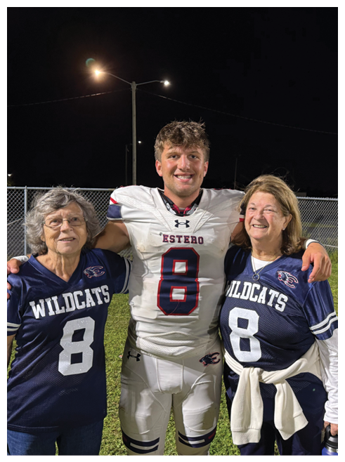 A person in a white football uniform with the number 8 stands smiling with arms around two people wearing blue Wildcats jerseys with the number 8 on a grassy field at night. Description generated by AI