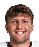 A person with short curly hair is smiling and wearing a white Wildcats sports jersey with red and blue stripes on the sleeves. Description generated by AI