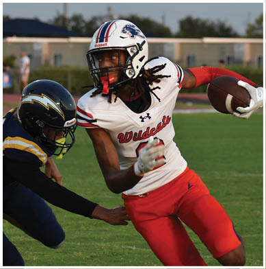 Two people in football uniforms are engaged in a play on a grassy field, with one person holding the ball and evading the other. Description generated by AI