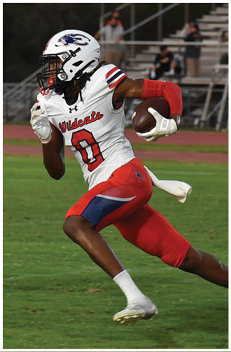 A person wearing a white football uniform with red and blue accents is running on a grassy field while holding a football. Description generated by AI