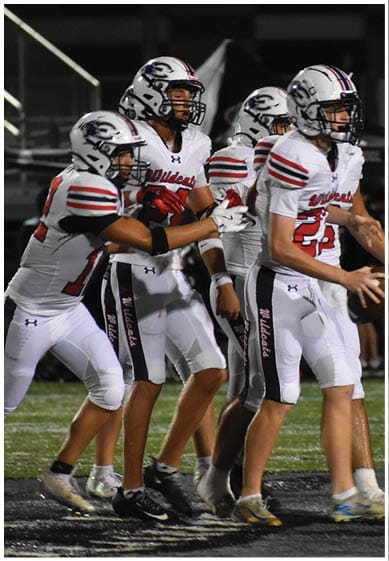 People wearing football uniforms with “W Wildcats" on the pants are standing closely together on a field. Description generated by AI